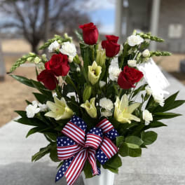 Red roses and white lilies in a white vase with an American flag ribbon