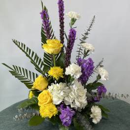 Yellow roses, white carnations, and purple flowers in a tall arrangement
