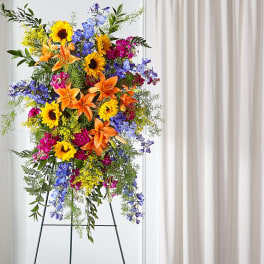 Tall standing floral spray with sunflowers, lilies, and blue flowers