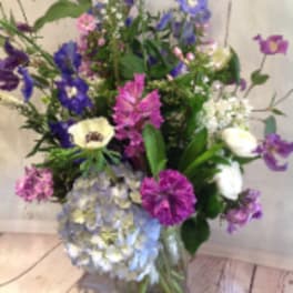 Tall mixed bouquet of purple, blue, pink, and white flowers in a clear glass vase