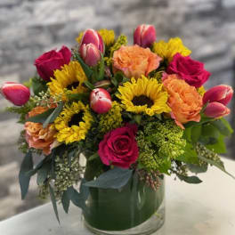 Mixed bouquet in a glass vase with roses, sunflowers, tulips, and carnations