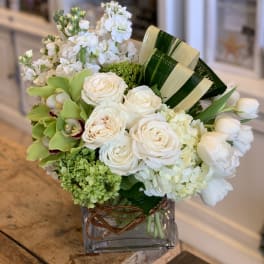 White roses and green orchids arranged in a square glass vase