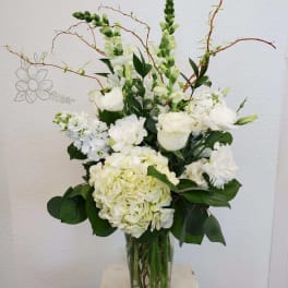 White floral arrangement in a clear glass vase with tall branching stems