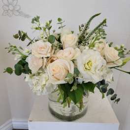 Cream roses and white blooms arranged in a clear glass vase