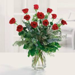 Red roses arranged in a clear glass vase with greenery
