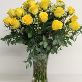 Yellow roses arranged in a clear glass vase with greenery