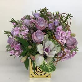 Lavender roses and pink flowers arranged in a yellow box