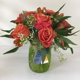 Coral and pink roses in a green glass vase with mixed greenery