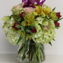 Mixed bouquet of hydrangeas, orchids, lilies, and roses in a glass vase