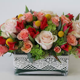 Mixed roses and yellow button flowers in a glass vase with lace trim