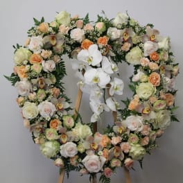 Heart-shaped floral wreath on an easel with white orchids and pastel roses