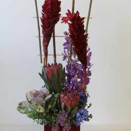 Tall tropical flower arrangement in a red container with bamboo accents