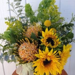 Bouquet of yellow sunflowers and mixed greenery in a clear vase