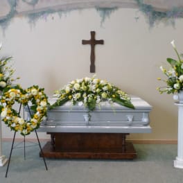 Funeral casket with white and yellow floral sprays and a heart wreath