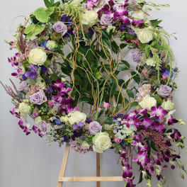 Large floral wreath on an easel with purple orchids and white roses