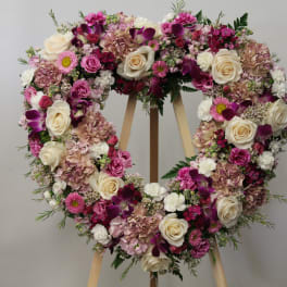 Heart-shaped floral wreath with pink, white, and purple flowers on an easel