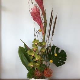 Tall tropical arrangement with pink blooms in a white vase