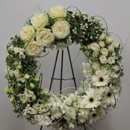 White floral wreath on a black stand with roses and daisies
