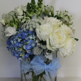 White roses and blue hydrangeas in a square glass vase with a blue bow