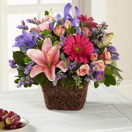 Mixed bouquet in a woven basket with pink, purple, and peach flowers