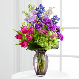 Bouquet of pink tulips, purple flowers, and green hydrangeas in a purple vase