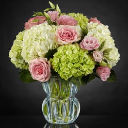 Pink roses and green-white hydrangeas arranged in a clear glass vase