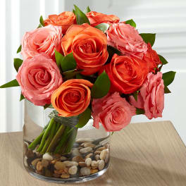 Pink and orange roses arranged in a clear glass vase with pebbles