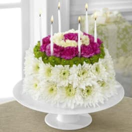 Tiered floral cake with white, pink, and green flowers and lit candles