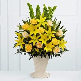 Yellow lilies and pale roses arranged in a cream vase