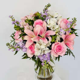 Pink lilies and roses arranged in a clear glass vase with white and lavender flowers