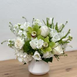 White floral arrangement in a white vase with green orchids and tulips