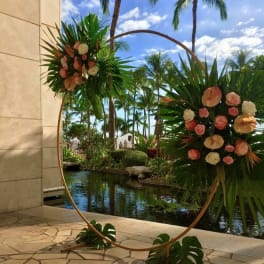 Two floral arrangements on a circular stand beside a tropical pool