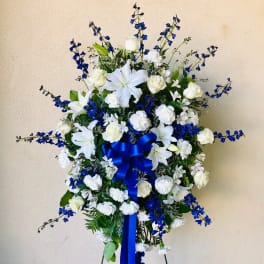 Standing floral spray of white lilies and roses with blue flowers and ribbon