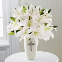White lilies arranged in a tall vase with a cross emblem