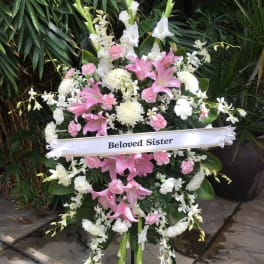 Standing funeral spray with pink lilies and white flowers, labeled "Beloved Sister"