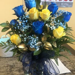 Blue and yellow roses arranged in a glass vase with a dark ribbon