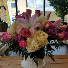Pink lilies and roses arranged with cream hydrangeas in a white vase