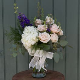 Bouquet of pale pink roses, white hydrangea, and purple flowers in a glass vase