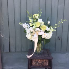 White and pale green floral arrangement in a glass vase with a ribbon