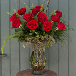 Red roses arranged in a clear glass vase with fern accents