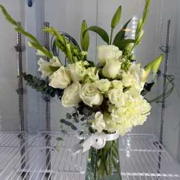 Tall arrangement of white roses, lilies, and hydrangea with green buds in a clear glass vase.
