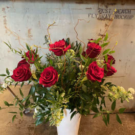 Red roses arranged in a white vase with greenery