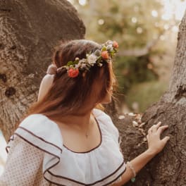 Woman wearing a floral crown and white dress standing by a tree