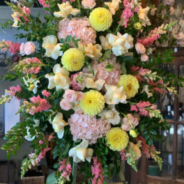 Large pastel floral arrangement on an easel with pink, yellow, and white blooms