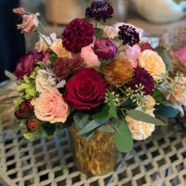 Mixed bouquet of roses and dark blooms in a gold vase