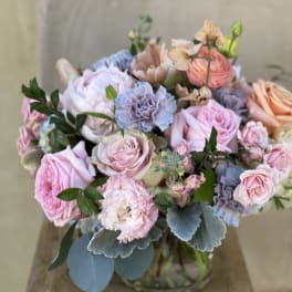 Pastel bouquet of roses, carnations, and blue flowers in a glass vase