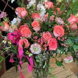 Pink roses and mixed blooms arranged in a clear glass vase with ribbon