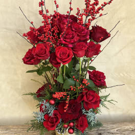 Tall arrangement of red roses with berry branches in a gold vase