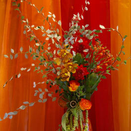 Tall floral arrangement in a red vase with orange and yellow blooms