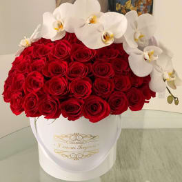 Round white hatbox packed with red roses and topped with white orchids on a glass table